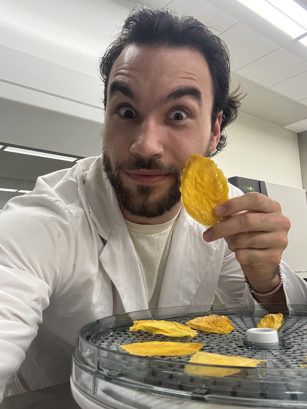 Josh in the lab holding a slice of dried mango over a dehydrator tray